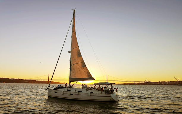 Sailboat on Tagus River at sunset with Lisbon's 25 de Abril Bridge in the background.