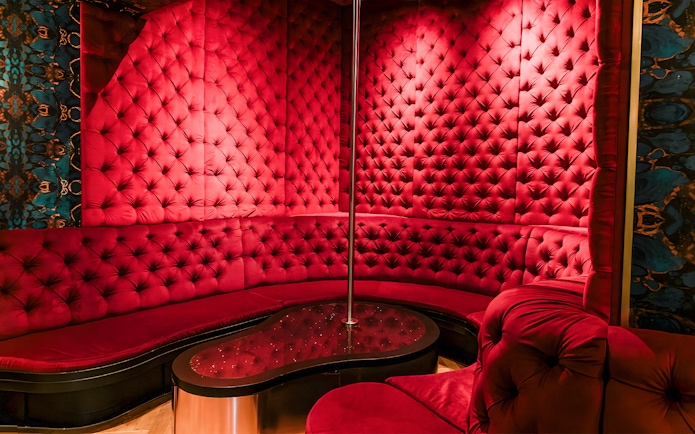 Luxurious red velvet seating area with a pole at Tour de BonTon strip club.