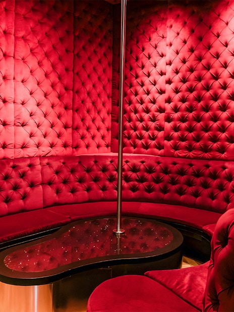 Luxurious red velvet seating area with a pole at Tour de BonTon strip club.