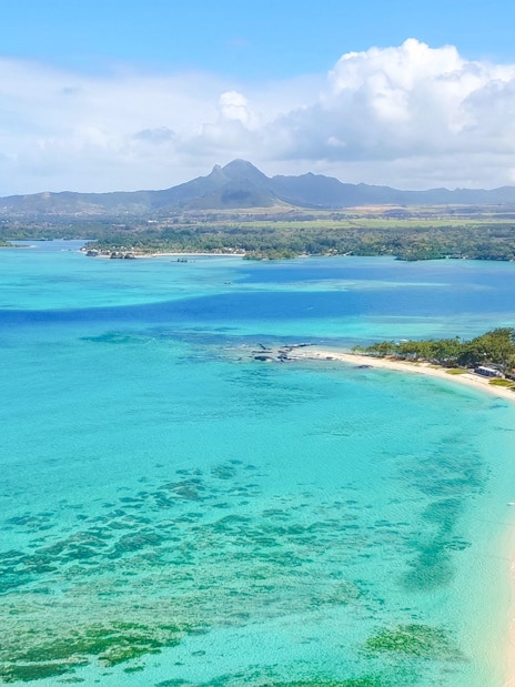 Aerial view of Mauritius coastline with turquoise waters and distant mountains on the Eastern Underwater Waterfall route.