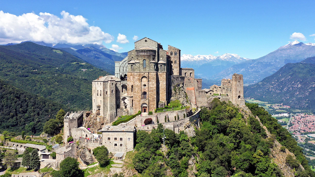 Sacra di San Michele abbey on a hilltop near Turin, Italy, with mountains in the background.