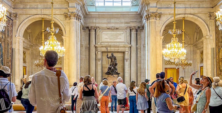 Visitors exploring the ornate hall of the Royal Palace of Madrid with chandeliers and statues.
