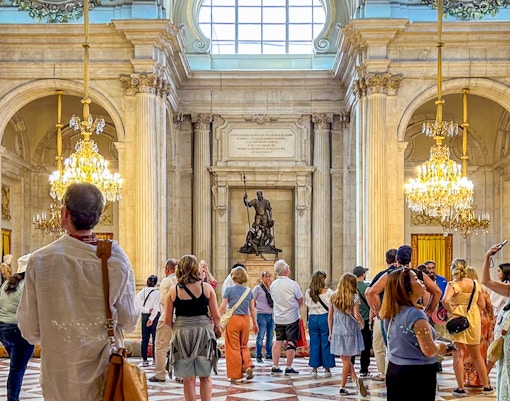 Visitors exploring the ornate hall of the Royal Palace of Madrid with chandeliers and statues.