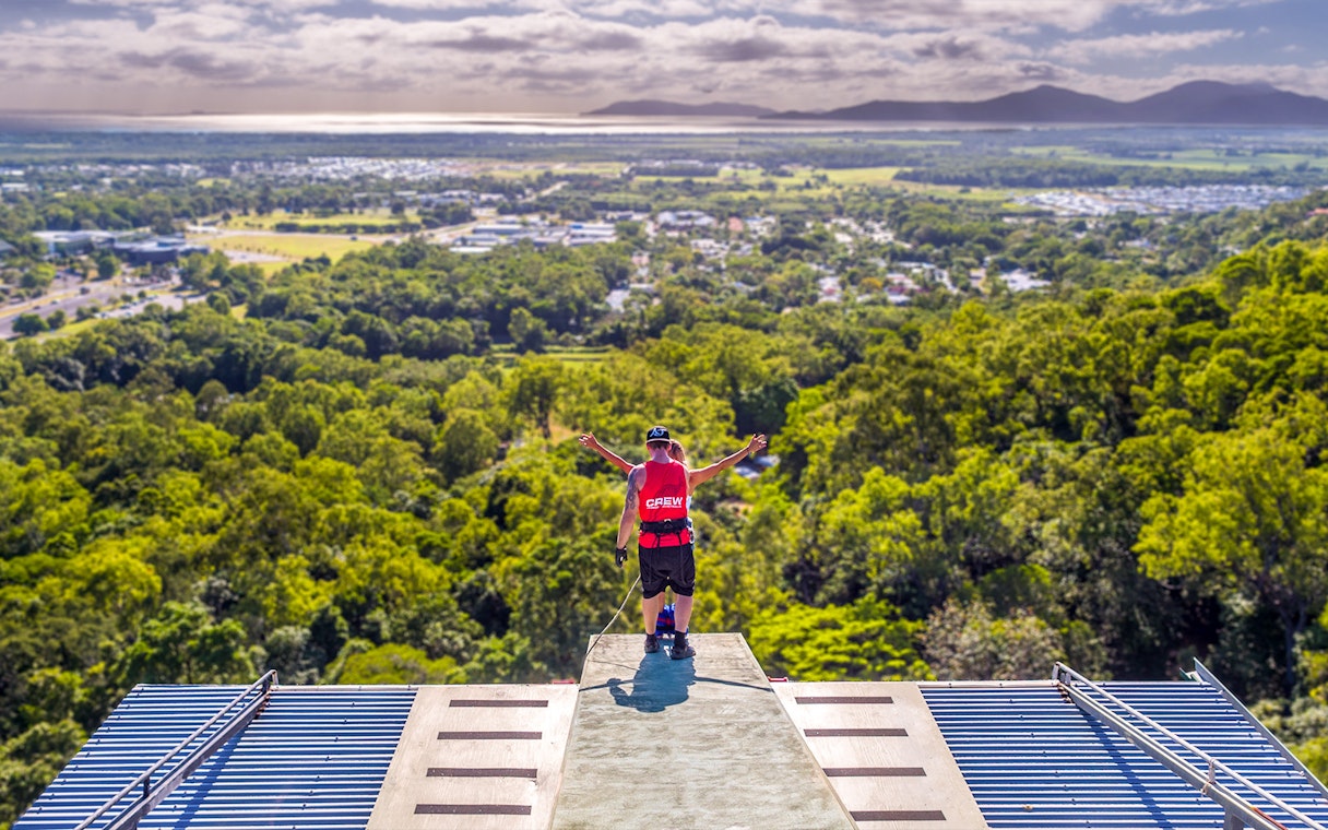Bungy jumper on platform overlooking Cairns landscape, preparing to jump.