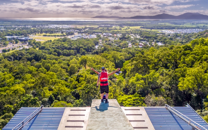 Bungy jumper on platform overlooking Cairns landscape, preparing to jump.