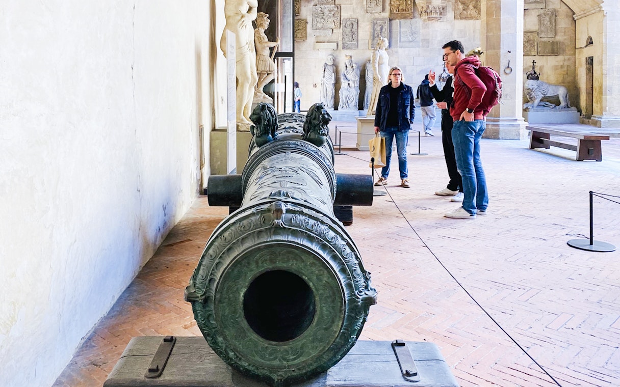 Visitors exploring sculptures and a historic cannon at Bargello Museum, Florence.