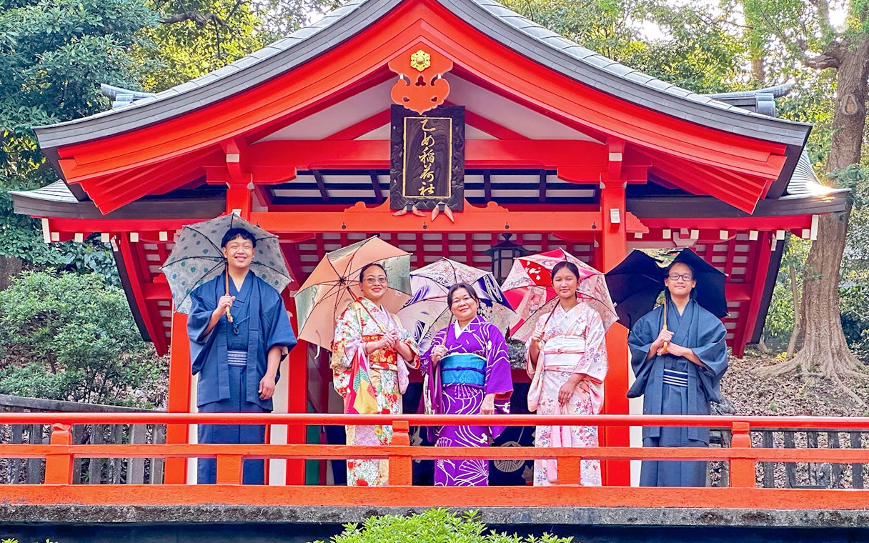 Visitors in traditional attire with umbrellas in front of a historic Japanese temple.