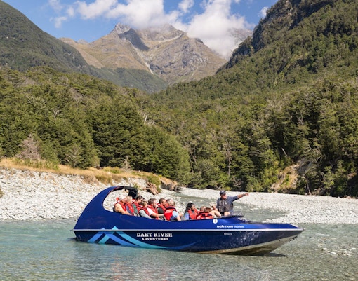 Jet boat on Dart River with tourists, surrounded by lush forest and mountains, New Zealand.