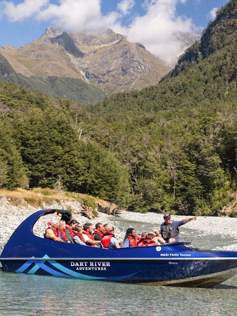 Jet boat on Dart River with tourists, surrounded by lush forest and mountains, New Zealand.
