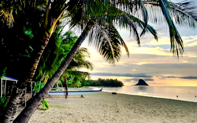 Secret Island Beach at sunset with palm trees and a canoe, Kualoa Ranch, Hawaii.