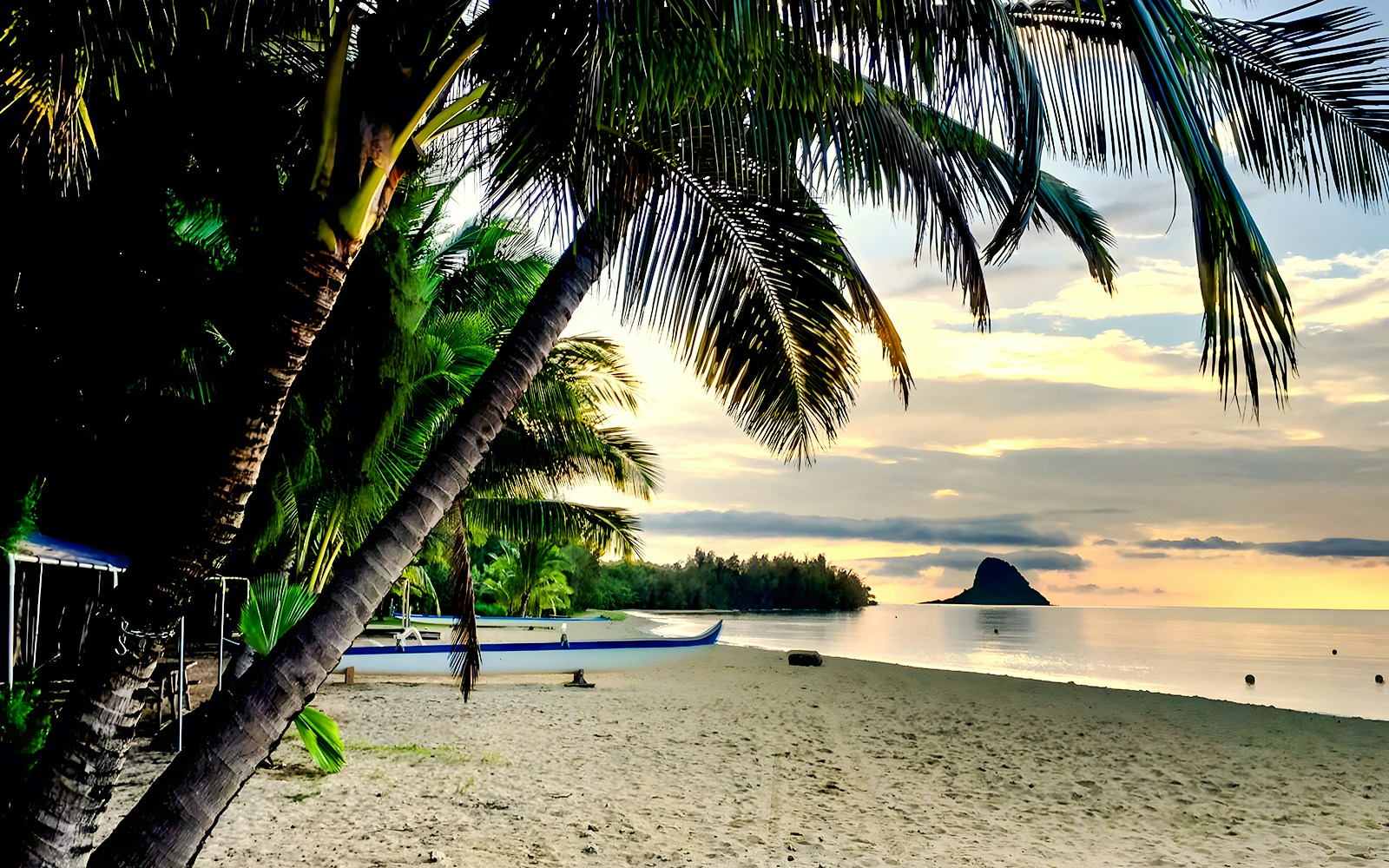 Secret Island Beach at sunset with palm trees and a canoe, Kualoa Ranch, Hawaii.