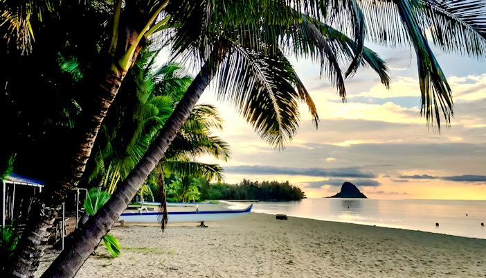 Secret Island Beach at sunset with palm trees and a canoe, Kualoa Ranch, Hawaii.