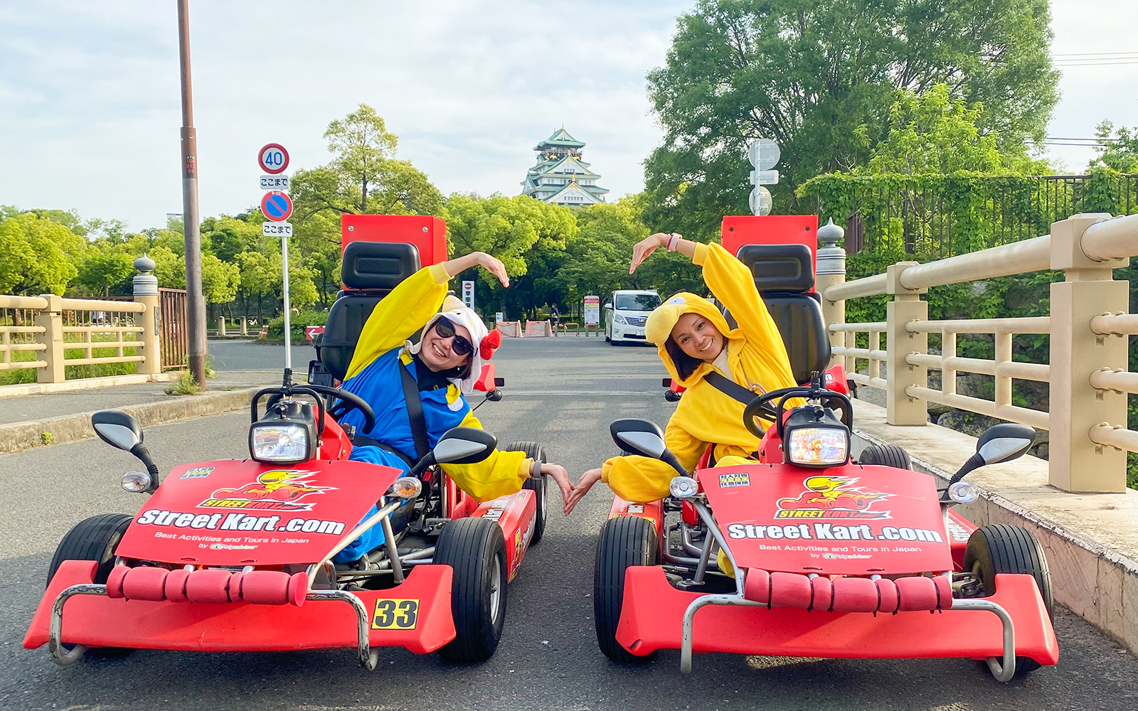 Go-kart riders in costumes pose on a street in Osaka Namba with Osaka Castle in the background.