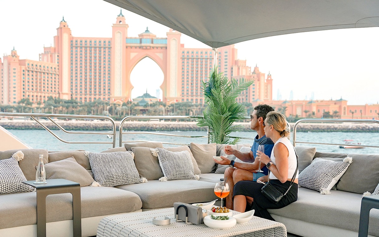Couple enjoying gourmet dining on a yacht with Atlantis, The Palm in Dubai in the background.