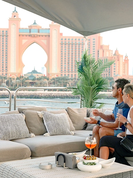Couple enjoying gourmet dining on a yacht with Atlantis, The Palm in Dubai in the background.