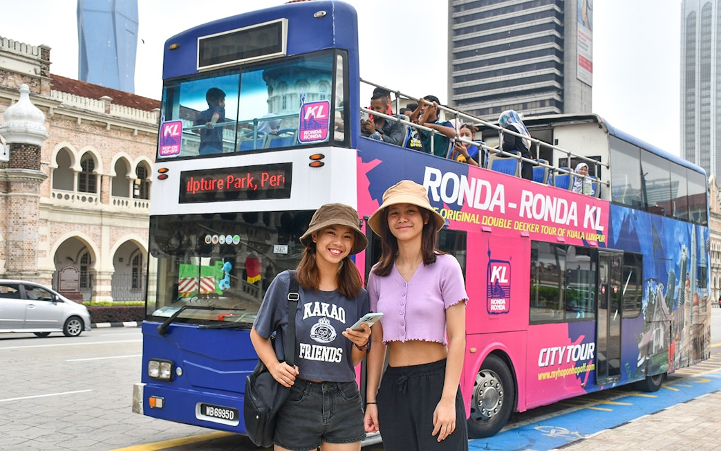 Hop-On Hop-Off bus tour in Kuala Lumpur with passengers and city landmarks in the background.