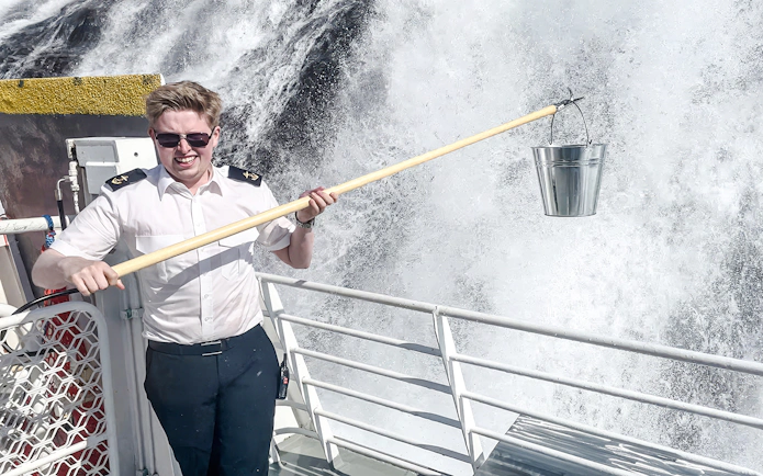 Boat crew member collecting waterfall water on Geiranger Fjord tour.