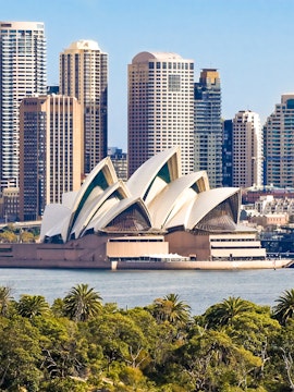 Sydney Opera House with city skyline in the background, viewed from across the harbor.