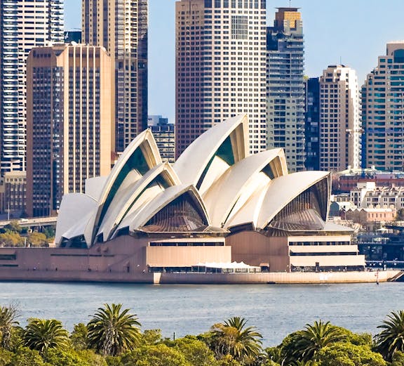 Sydney Opera House with city skyline in the background, viewed from across the harbor.