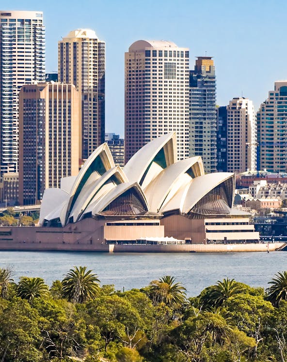 Sydney Opera House with city skyline in the background, viewed from across the harbor.