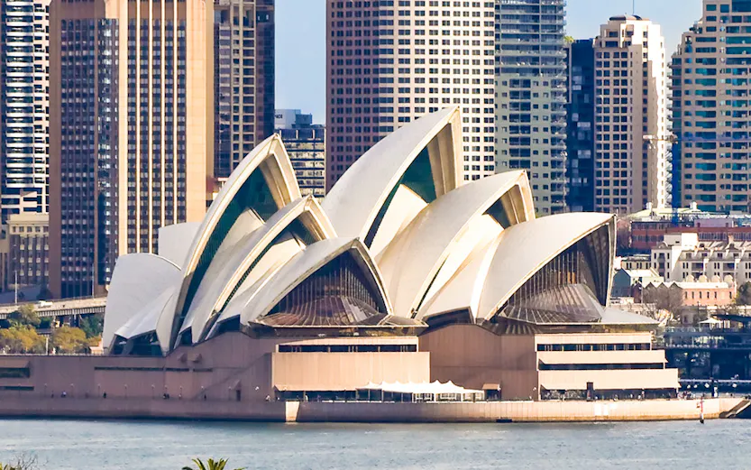 Sydney Opera House with city skyline in the background, viewed from across the harbor.