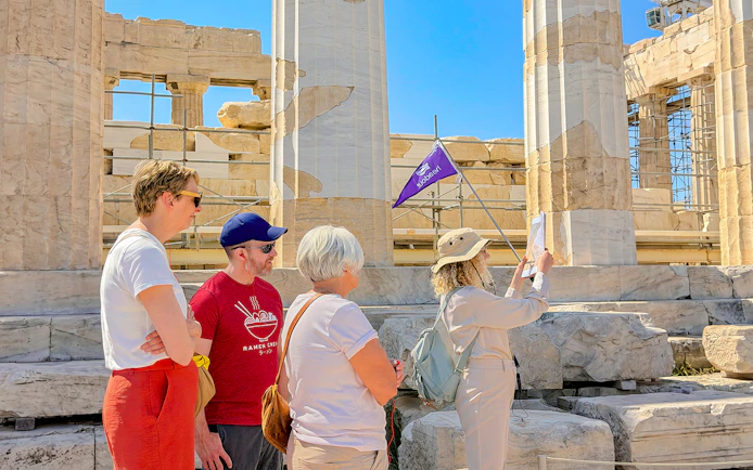 Tour group exploring the Acropolis in Athens with a guide holding a flag.