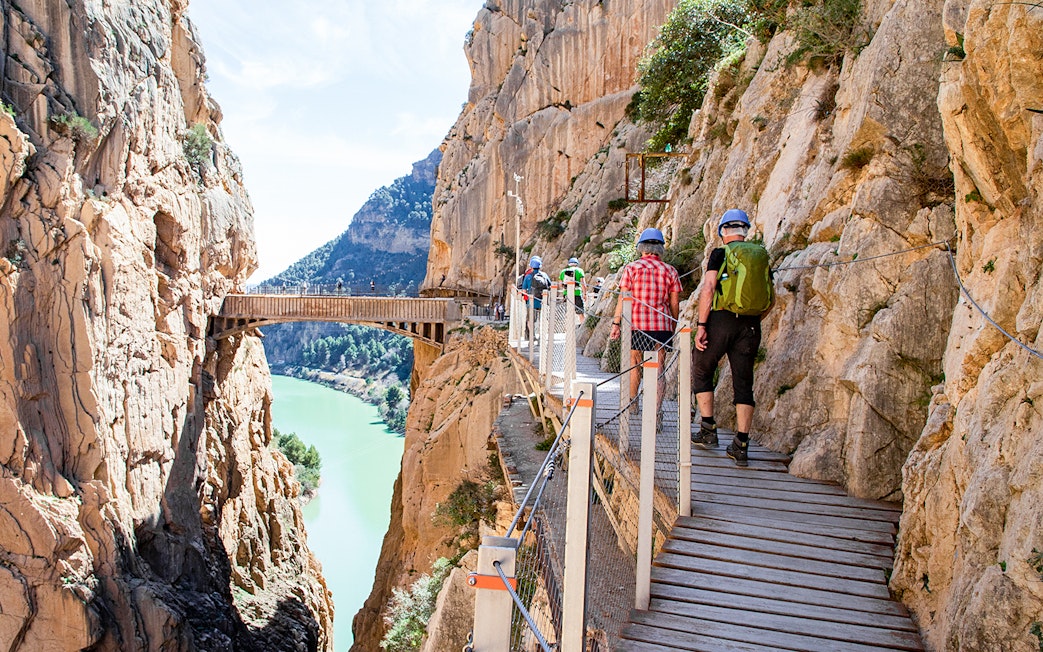 Hikers on Caminito del Rey trail in Málaga, Spain, walking along a cliffside path.