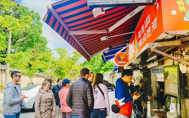 Tourists enjoying street food at a vendor stall during a Seoul Street Food Walking Tour.