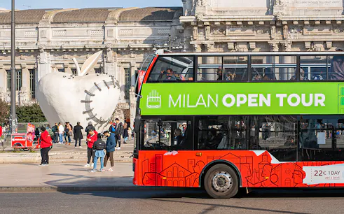 Hop-on hop-off bus near Milan's Central Station with apple sculpture in background.