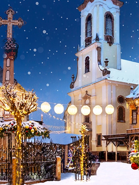 Szentendre Christmas Market with festive lights, snow-covered trees, and historic church.
