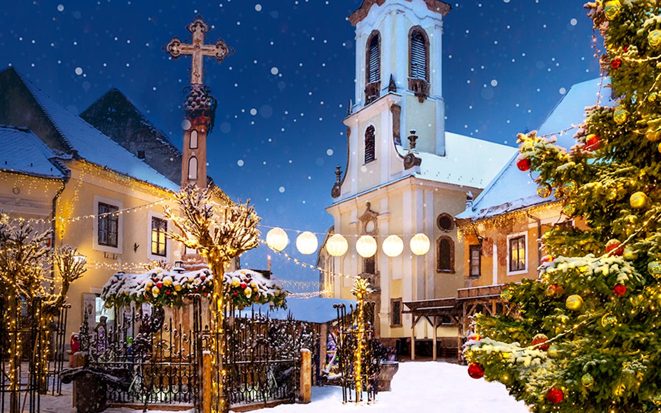 Szentendre Christmas Market with festive lights, snow-covered trees, and historic church.