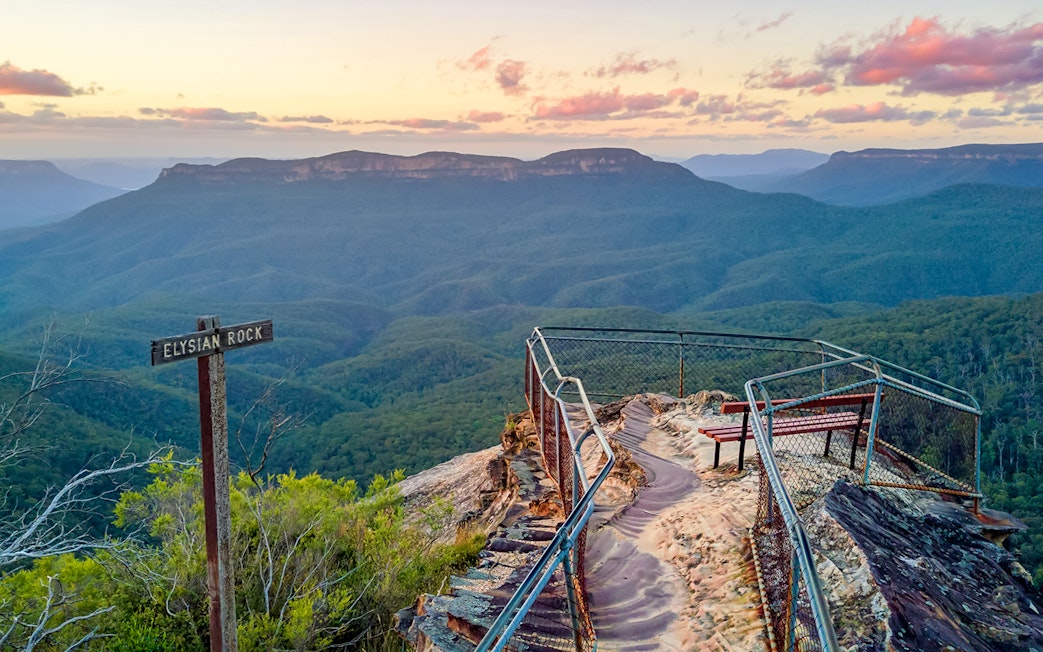 Elysian Rock viewpoint overlooking Blue Mountains at sunset, with a sign and railing.