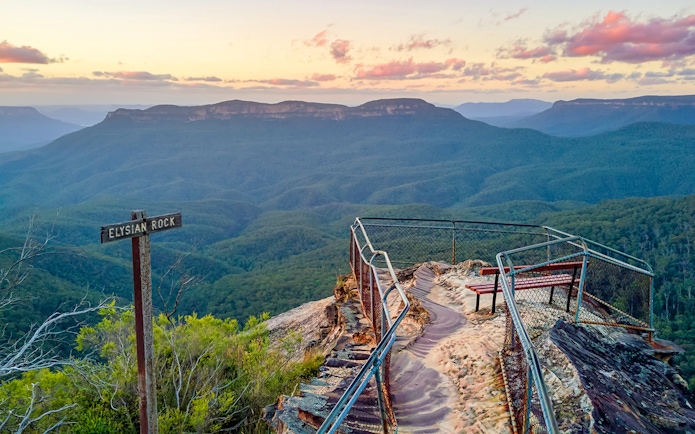 Elysian Rock viewpoint overlooking Blue Mountains at sunset, with a sign and railing.