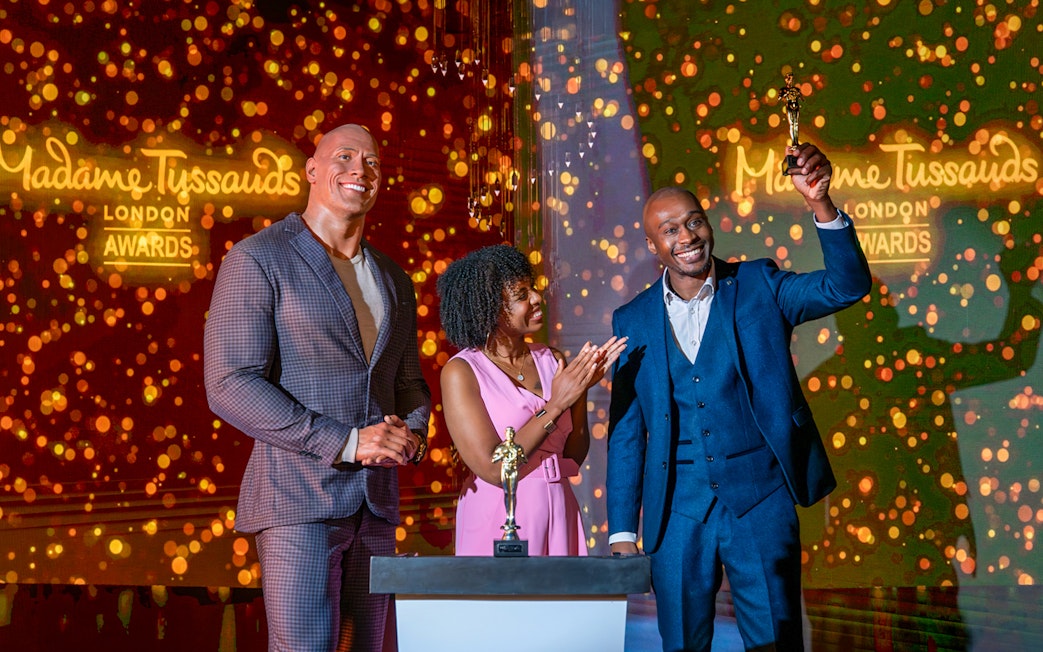 Wax figure of The Rock at Madame Tussauds London with two people celebrating an award.