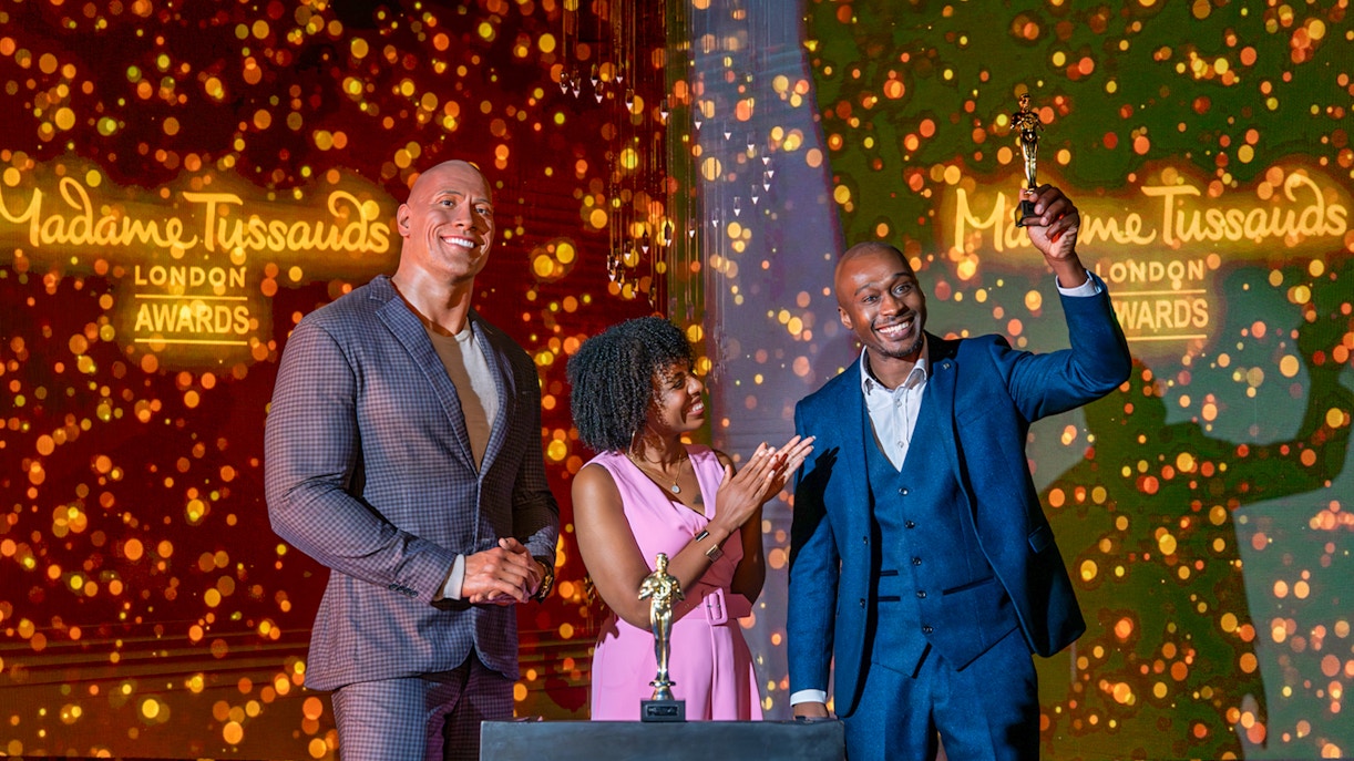 Wax figure of The Rock at Madame Tussauds London with two people celebrating an award.