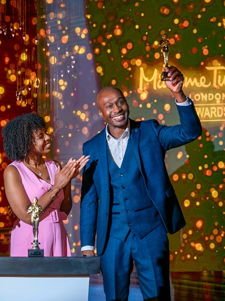 Wax figure of The Rock at Madame Tussauds London with two people celebrating an award.