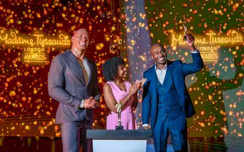 Wax figure of The Rock at Madame Tussauds London with two people celebrating an award.