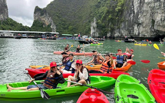 Kayakers enjoying Ha Long Bay on La Casta Day Cruise with limestone cliffs in the background.