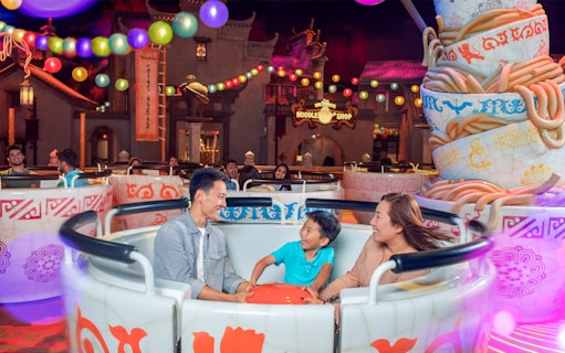 Family enjoying a teacup ride at Dubai Parks & Resorts, surrounded by colorful lights.