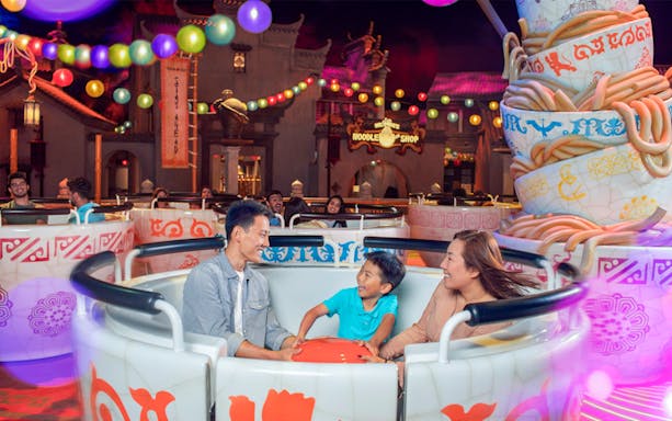 Family enjoying a teacup ride at Dubai Parks & Resorts, surrounded by colorful lights.