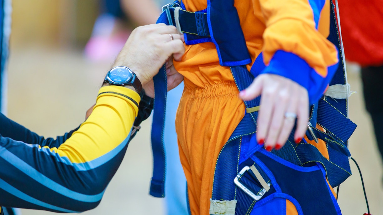 Instructor adjusting parachute suit straps for skydiving preparation.