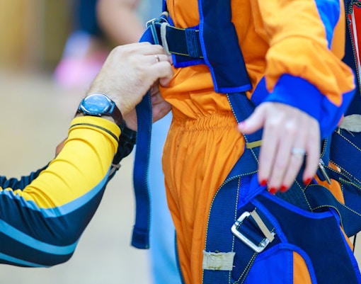 Instructor adjusting parachute suit straps for skydiving preparation.