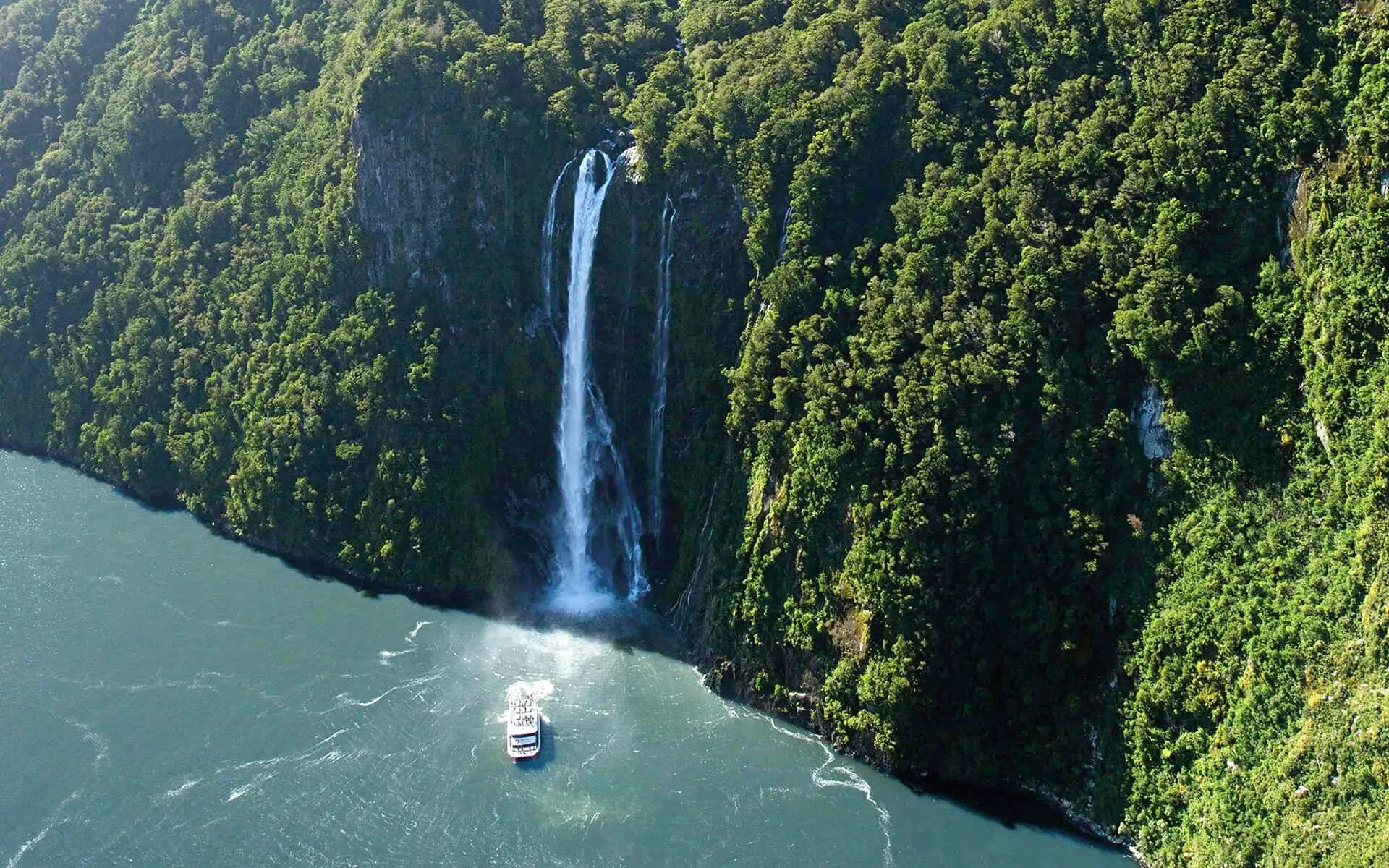 Cruise boat approaching waterfall in Milford Sound, New Zealand.
