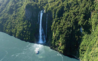 Cruise boat approaching waterfall in Milford Sound, New Zealand.