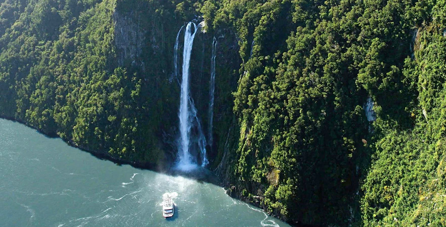 Cruise boat approaching waterfall in Milford Sound, New Zealand.