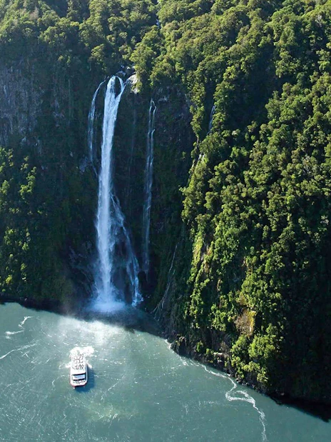 Cruise boat approaching waterfall in Milford Sound, New Zealand.