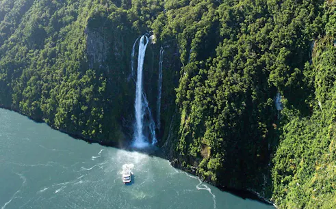 Cruise boat approaching waterfall in Milford Sound, New Zealand.