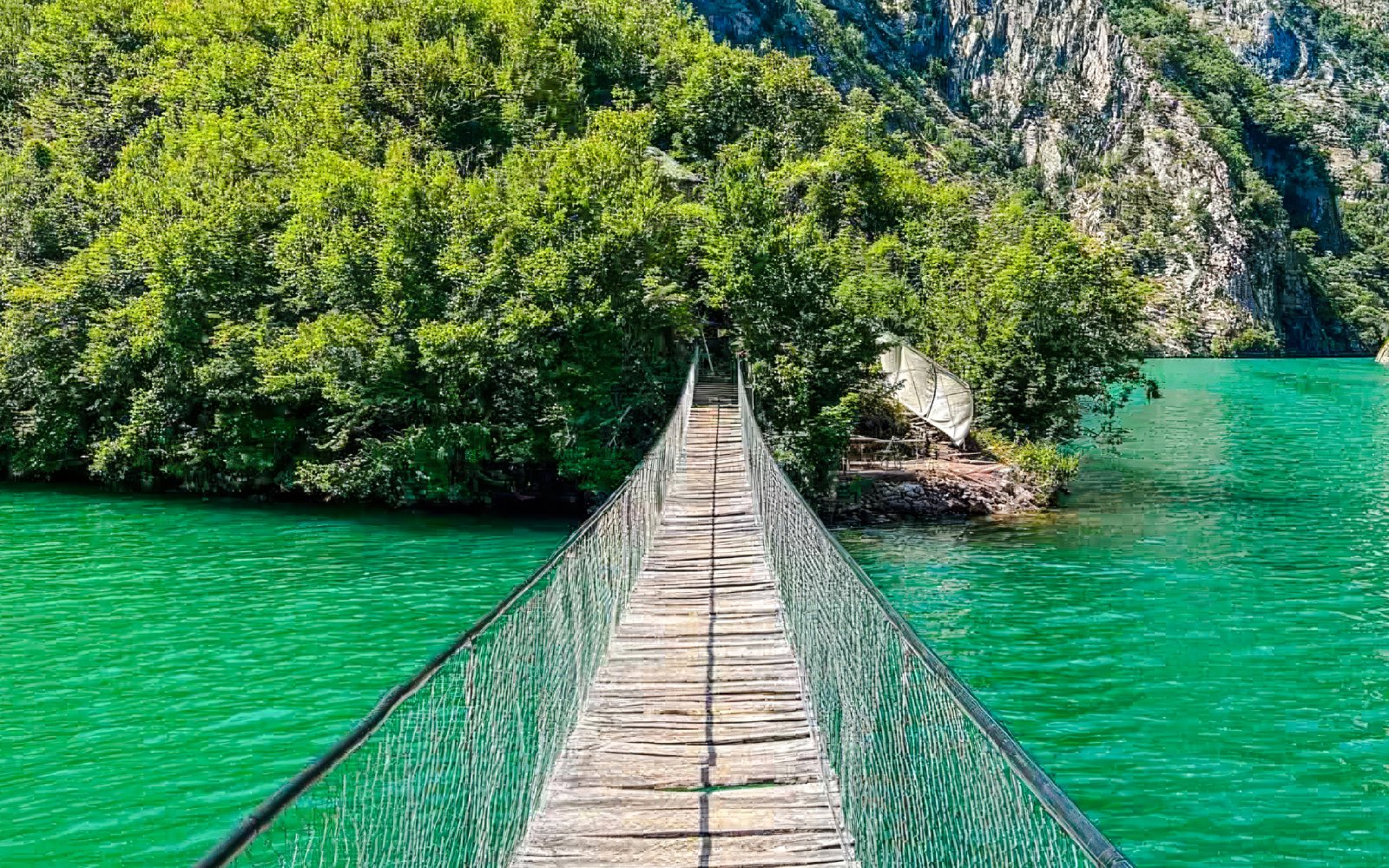 Bridge over the Shala River with lush greenery and turquoise water in the background.
