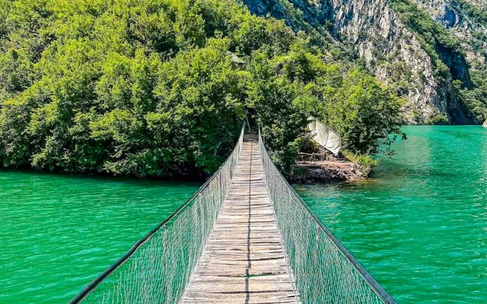 Bridge over the Shala River with lush greenery and turquoise water in the background.