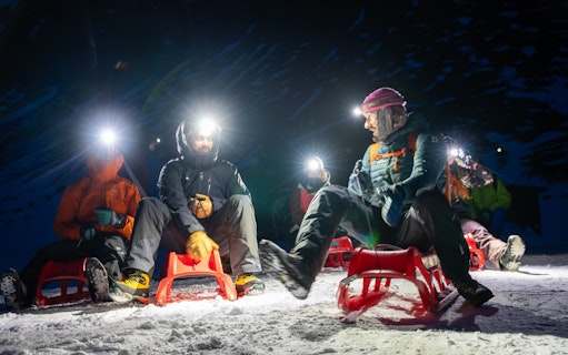 Group sledding at night with headlamps in snowy Interlaken.